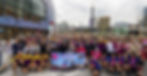 The finishing reception at Kai Tak Stadium, people smiling and excited holding a banner reading "Congrats John & Jo, Beijing to Hong Kong."